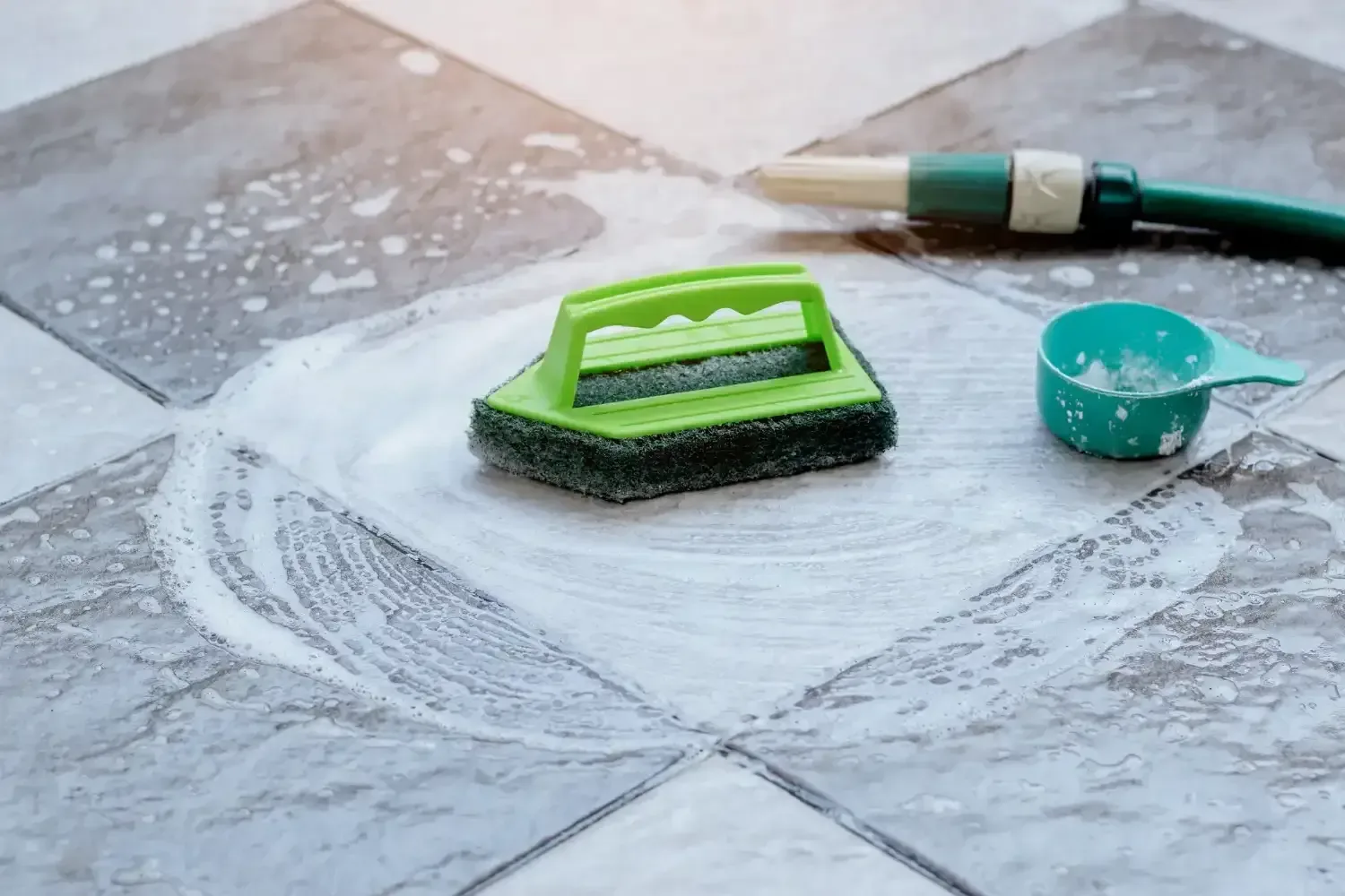 A green sponge is being used to clean a tile floor.